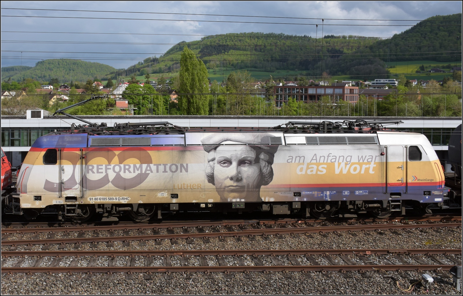 185 589 mit 500 Jahre Reformation ist die zweite Lok eines durchfahrenden Zuges hinter 185 585, beide Rheincargo, in Frick. April 2022.