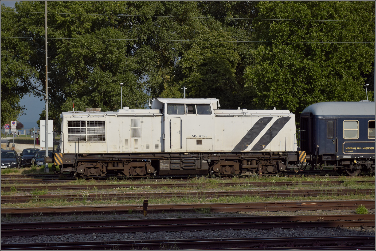 92 54 2745 903-1 CZ-RTTS lautet die Nummer der nach Tschechien eingebürgerten V 100 Ost. Gerade soll sie die Wagen des Bohemian Classic Express auf das Gleis am ehemaligen SBB-Güterschuppen bringen, während kurz ein Durchblick zum See aufblitzt. Konstanz, August 2026.