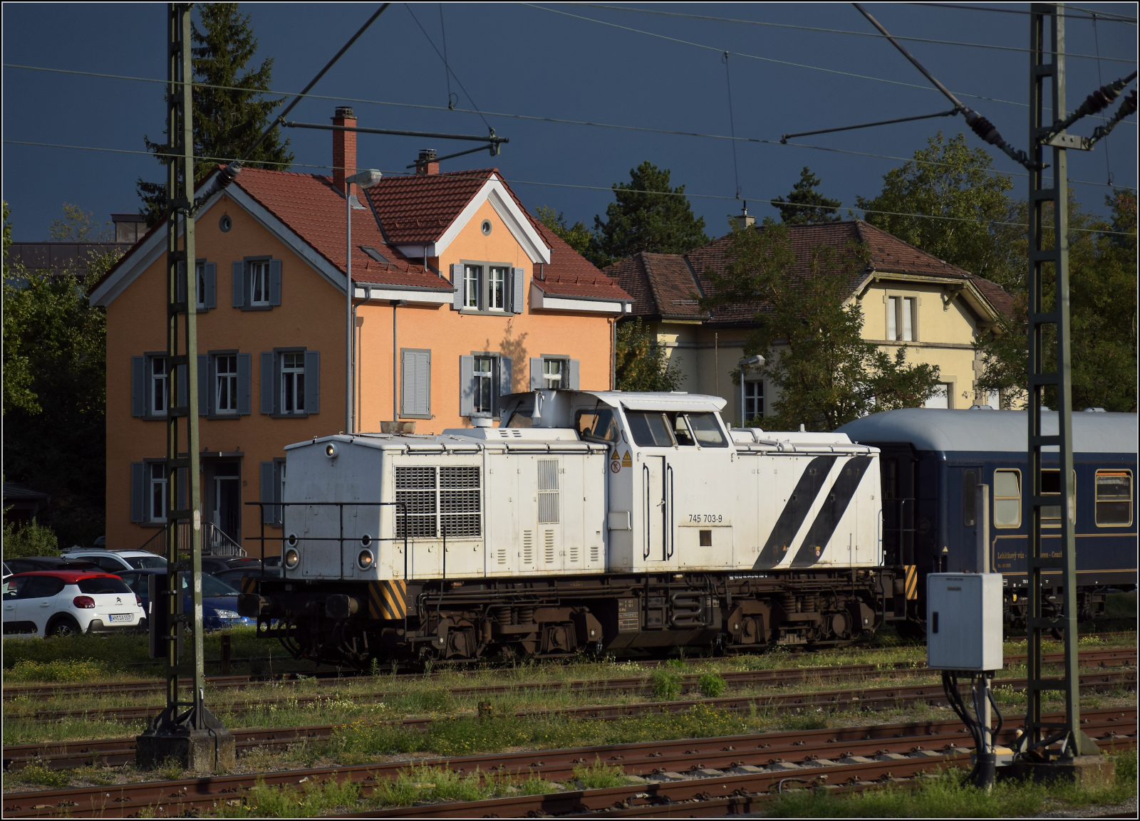92 54 2745 903-1 CZ-RTTS lautet die Nummer der nach Tschechien eingebürgerten V 100 Ost. Gerade soll sie die Wagen des Bohemian Classic Express auf das Gleis am ehemaligen SBB-Güterschuppen bringen und fährt an den beiden Gebäuden des Schweizer und deutschen Zolls vorüber. Konstanz, August 2026.