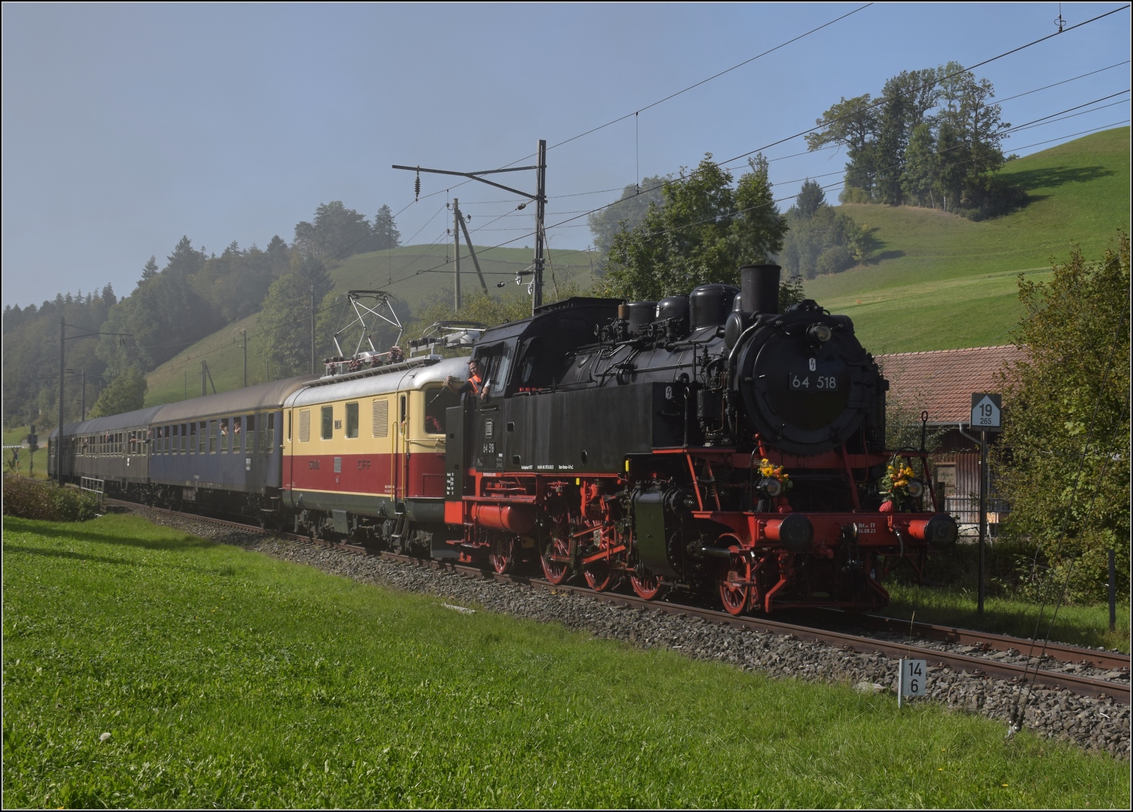 Dampftage Huttwil mit frisch genesenem Bubikopf. 

64 518 und Re 4/4 I 10034 mit zwei Silberlingen und einem erstklassigen Schnellzugwagen der DB kommt in Drrenroth an. Oktober 2023