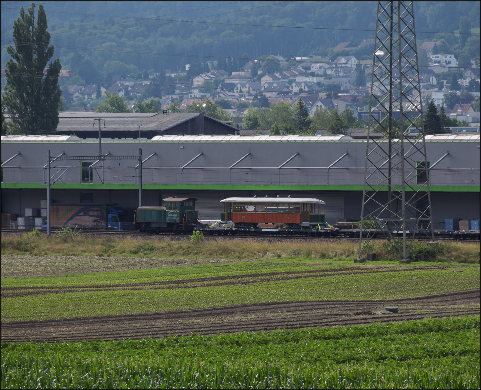 Das Transportgut ist Bi 369, ein Wagen der Genfer Strassenbahn und am Zugschluss der Tm IV 232 164 durch Buchs ZH nach Otelfingen. Juli 2023.