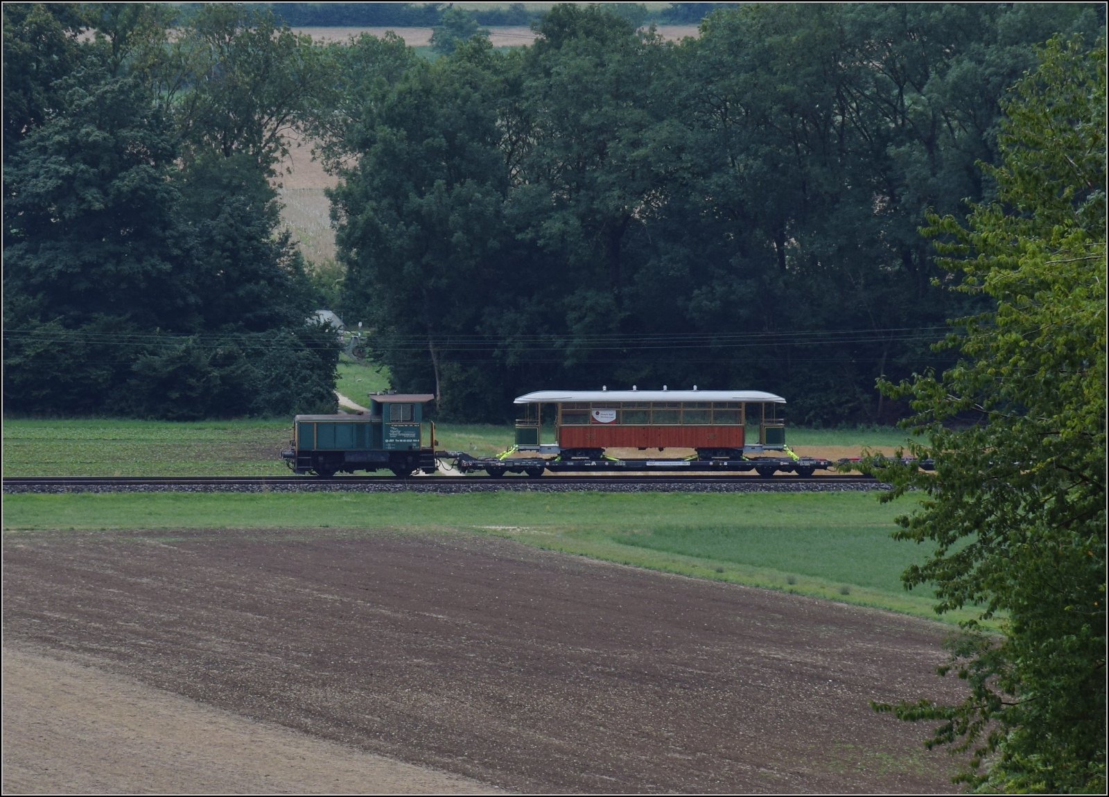 Der Zugschluss mit dem Transportgut, einem Wagen der Genfer Strassenbahn und Tm IV 232 164 bei Oberbuchsiten. Juli 2023.