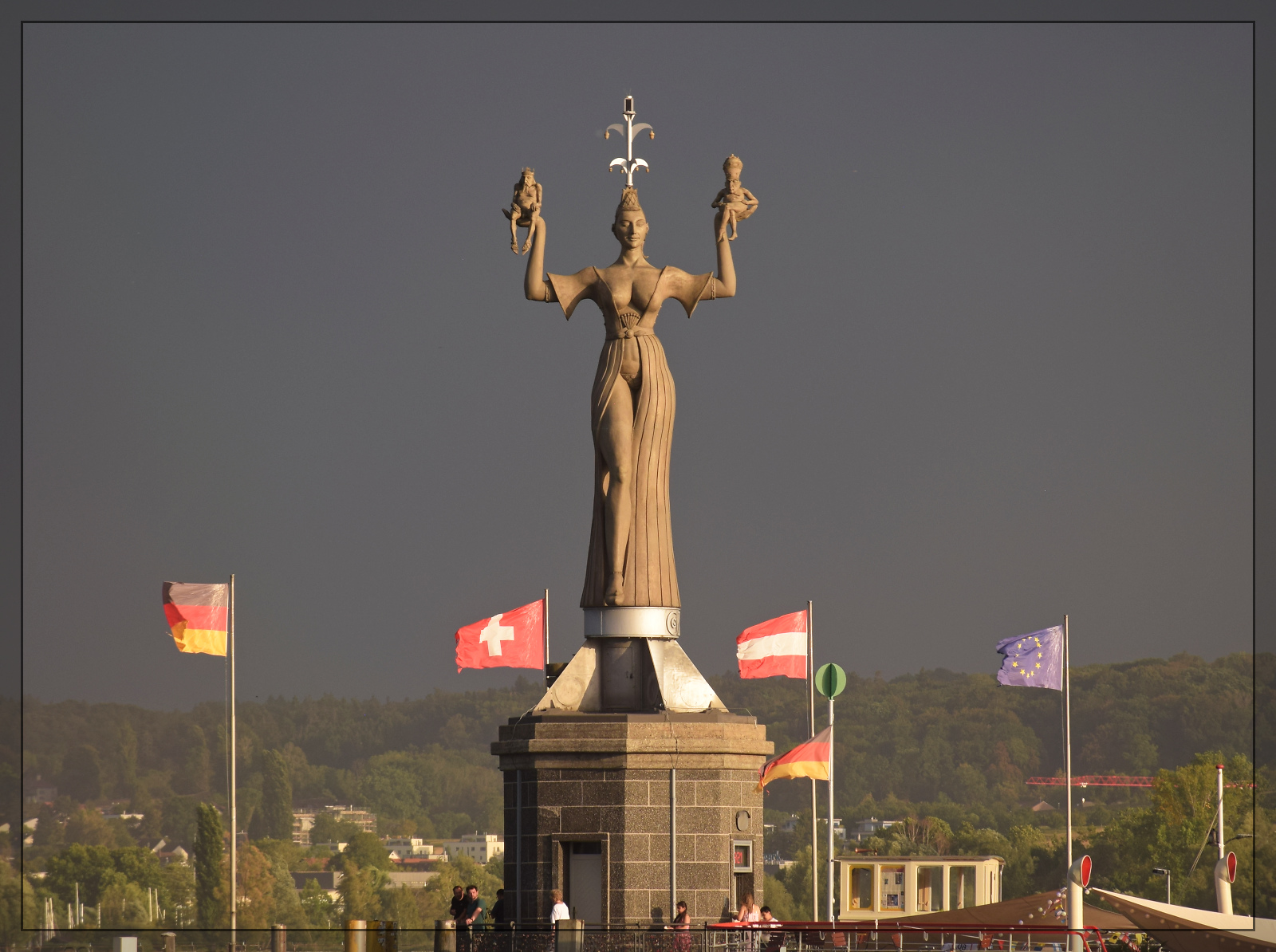 Die Sonne lugt bereits unter einem einem aufkommenden Gewitter hindurch und beleuchtet Imperia in der Hafeneinfahrt von Konstanz. August 2026.