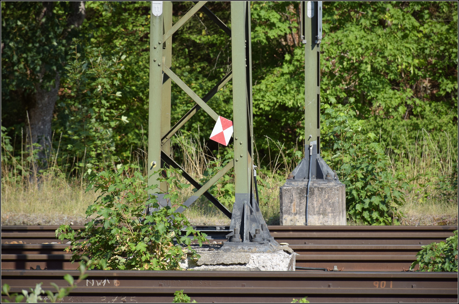 Mastschluss aber nicht Zugschluss, wie uns hier die in den Masten geflogene Zugschlusstafel fälschlicherweise verkünden will. Vielleicht will die Zugschlusstafel aber auch auf das Lebensende der Oberleitungsanlagen hinweisen. Tatsächlich sind die Masten und Fundamente aus den 1970er Jahren durchaus mit zweifelhafter Qualität installiert worden, wie man hier und andernorts unschwer erkennen kann. Hattingen, August 2026.