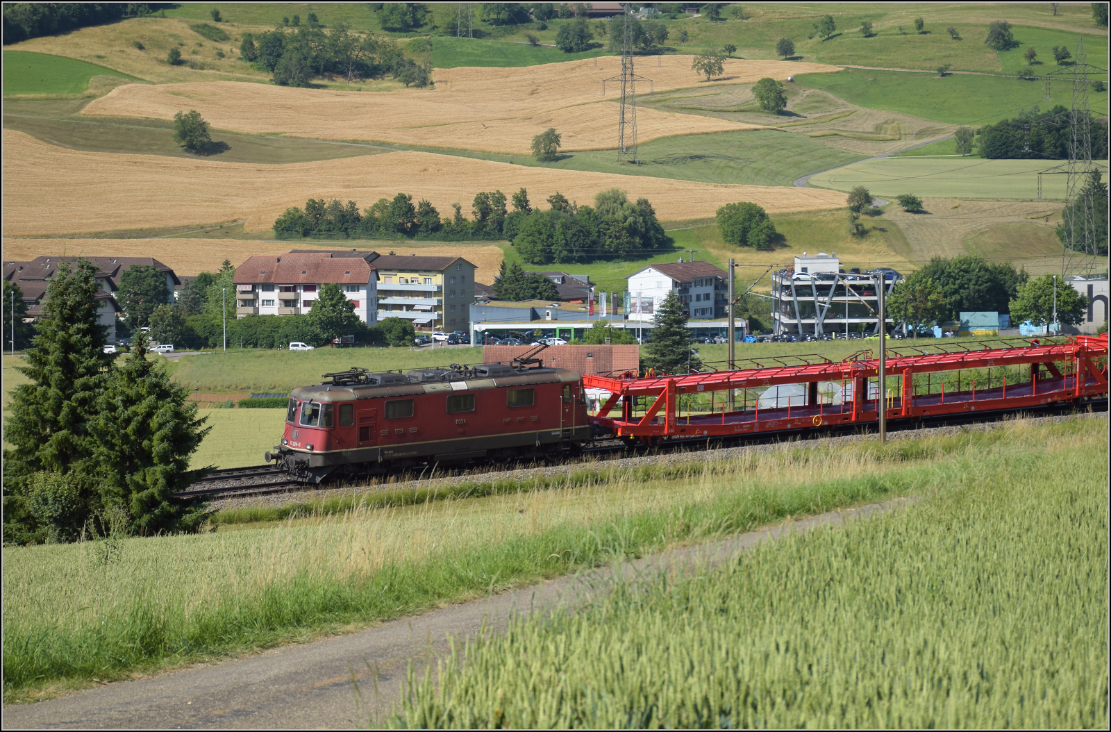 Re 4/4 II 11324 mit einem leeren Autozug bei Frick, Juni 2025.