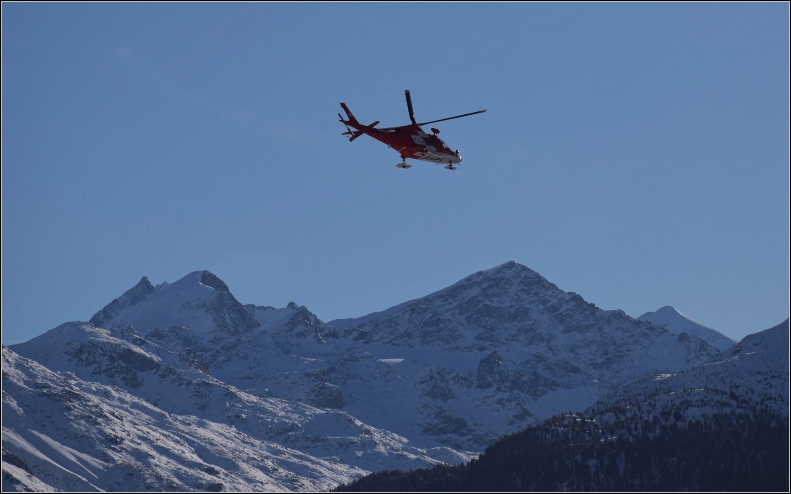 Rega Helicopter Agusta A109SP Da Vinci mit der Registrierung HB-ZRZ beim Flug über den Flughafen Samedan vor standesmässer Kulisse, namentlich die Bernina-Gruppe. Januar 2023.