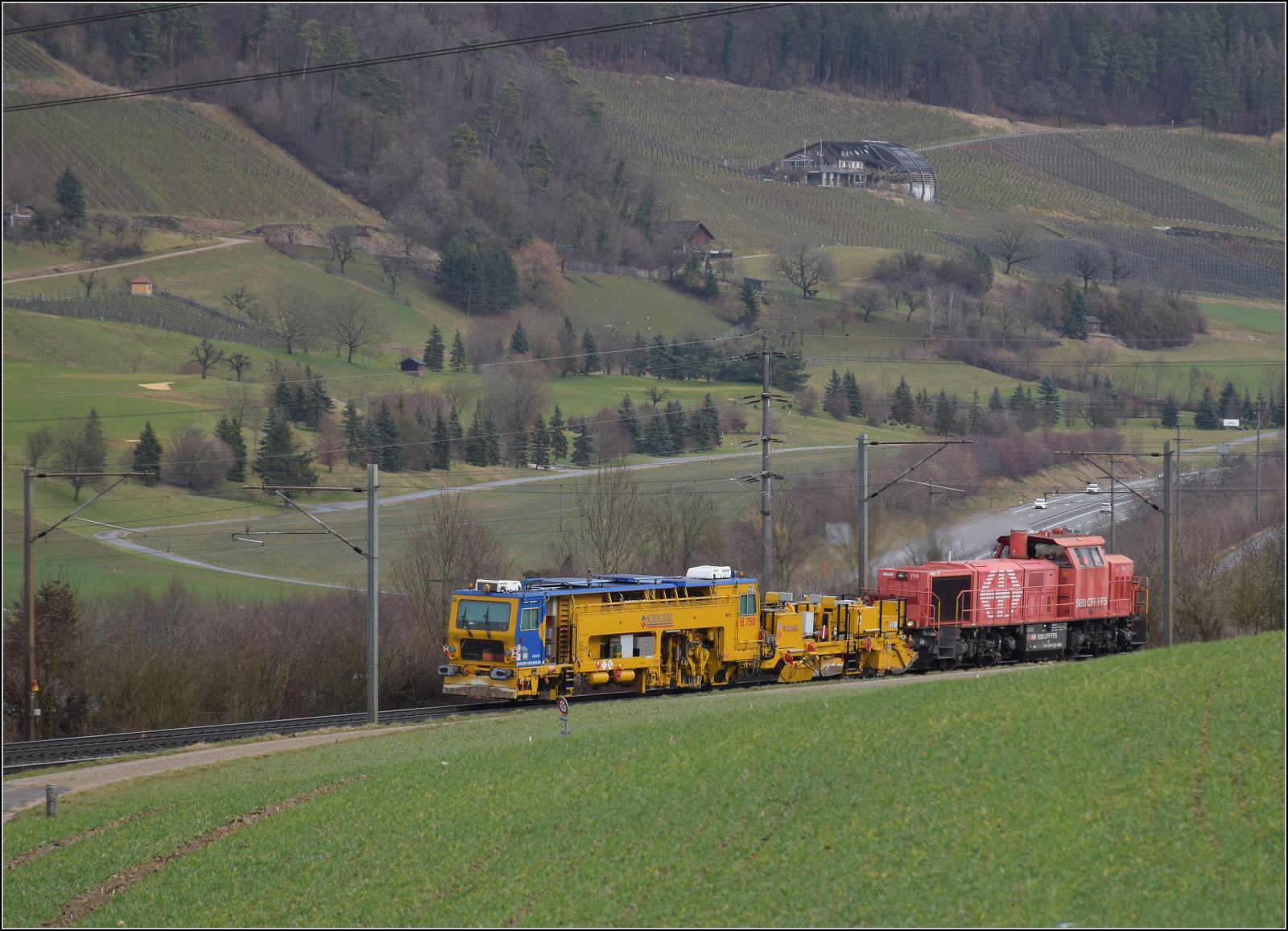 Schlechtwetter und ein Baustellendrama bei Frick. 

Am 843 020 der SBB Infrastruktur f�hrt mit einer Nivelier-Richt-Stopfmaschine B 758 von Scheuchzer (CH-SCHEU 40 85 9581 078) und dessen Anh�nger B 762 zum B�rsten des Schotterbetts in Richtung B�zberg. Februar 2026.