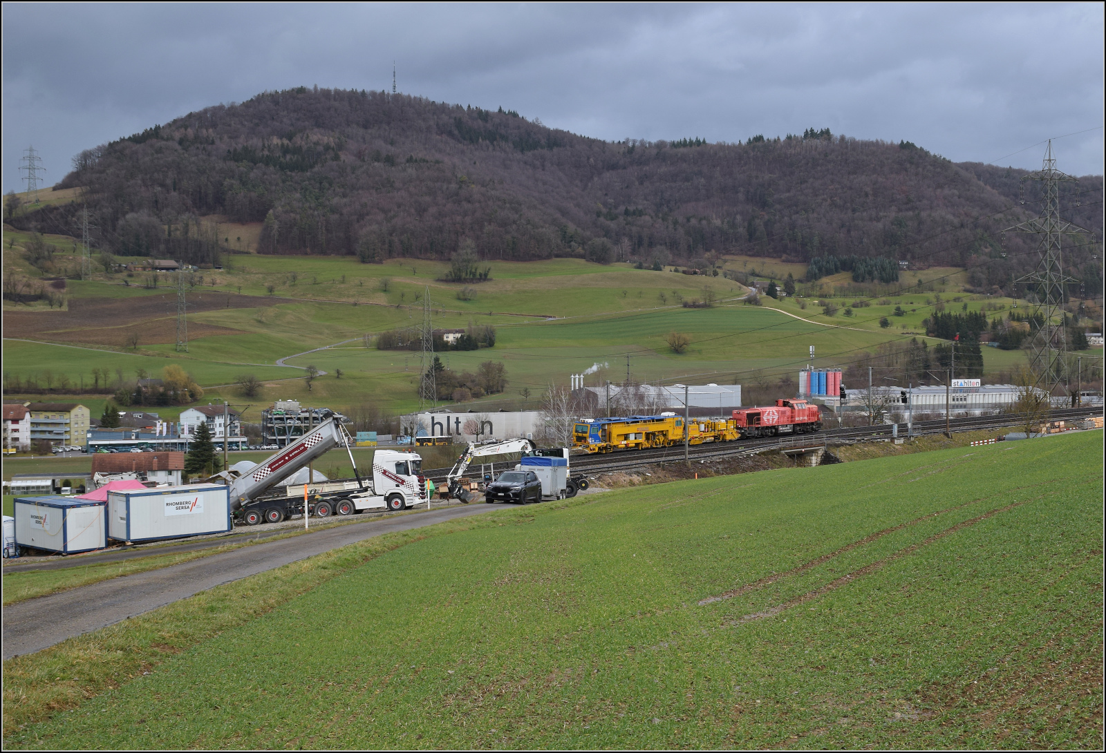 Schlechtwetter und ein Baustellendrama bei Frick. 

Am 843 020 der SBB Infrastruktur f�hrt mit einer Nivelier-Richt-Stopfmaschine VTmaas B 758 von Scheuchzer (CH-SCHEU 40 85 9581 078-4) und dessen Anh�nger B 762 zum B�rsten des Schotterbetts in Richtung B�zberg. In der Zwischenzeit hat man sich auf der Bereitstellungsanlage entschieden, das Momentum des Entladens f�r die Befreiungsaktion des LKW zu nutzen. Ernsthaft? Die werden doch den LKW in dieser instabilen Position des Sattelkippers rausziehen? Doch sie wollten tats�chlich...? Da kommen einem die vielen Youtube-Fail-Videos in den Kopf... Februar 2026.