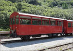 Der offene Personenwagen C 2353 der DFB im Dieselzug sieht recht unscheinbar und modern aus. De facto steckt hier ein wahrer  Methusalix  unter der modernen Haube. Der Wagen wurde 1889 von der SIG noch an die Jura-Bern-Luzern geliefert, die im Folgejahr in die Jura-Simplon eingegliedert wurde. Von 1903 bis 1971 war er den SBB zu Diensten, anschließend kam er via Ballenberg-Dampfbahn im Jahr 1993 zur DFB. 2015 gab es noch einen Schluck Zaubertrank, seitdem können auch Rollstuhlfahrer im Wagen mitfahren. Gletsch, August 2025.