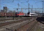 Viel los in Pratteln. Während 185 095 einen Güterzug zum Bözberg bringt, kommt von ebendort ein Interregio mit Re 4/4 II 11145, und RABe 521 024 fährt in den Bahnhof ein. März 2017.